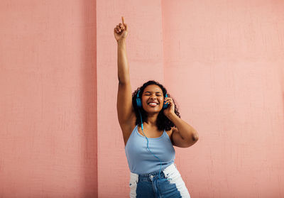 Cheerful woman listening music against wall