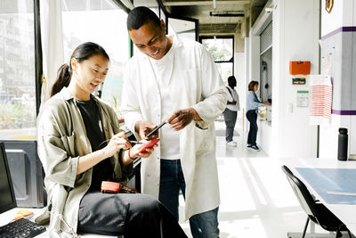 Smiling male and female technicians examining machine parts using multimeter at repair shop