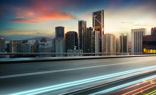 Illuminated city by buildings against sky during sunset