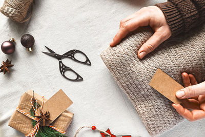 Woman's hands wrapping woolen sweater in craft recycled paper on the table with christmas decoration