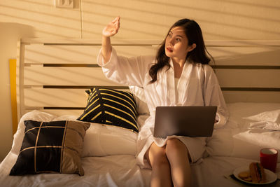 Young woman using phone while sitting on bed at home