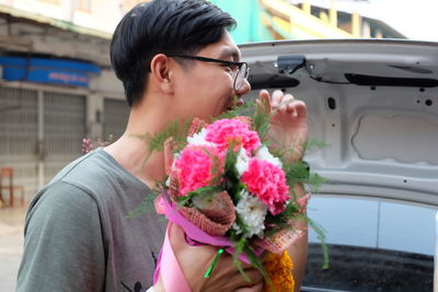 Smiling young man with bouquet at car trunk