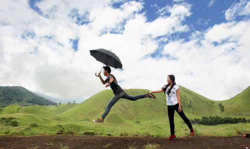 Woman pulling man leg while standing on hill against cloudy sky