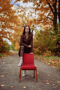 Young beautiful woman with old armchair on the country lane in autumn