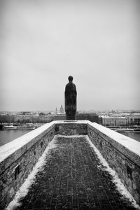 Rear view of statue on footpath against sky