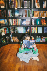 Girl reading book while sitting cross-legged on floor in bookstore