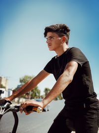 Side view of young man riding bicycle against sky