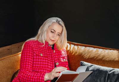Mature lady engrossed in a novel, relaxed on a mustard couch