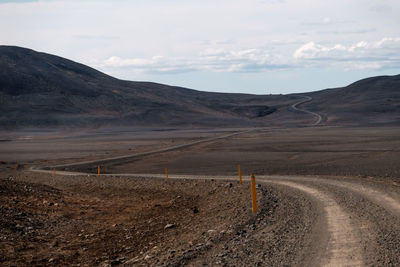 Dirt road leading towards mountains against sky