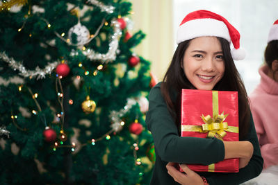 Portrait of smiling young woman holding christmas present at home