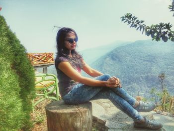 Young woman sitting on tree against sky