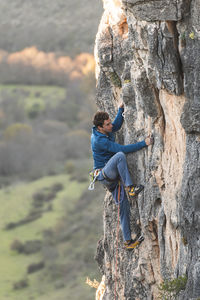 Man with safety harness clambering rock cliff