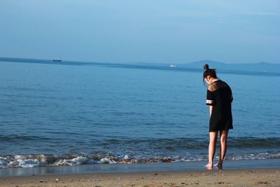 Woman standing at beach against sky