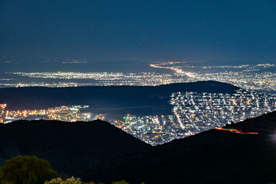 High angle view of illuminated city by sea against sky