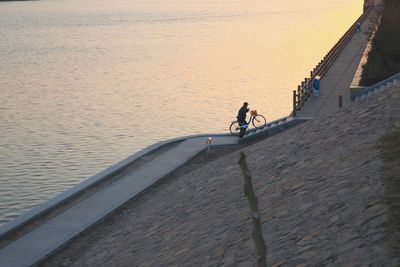 Man carrying bicycle on street by sea