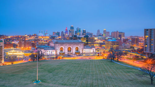 Illuminated buildings in city against blue sky