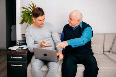 Young man with grandfather using laptop on sofa