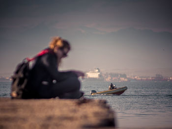 Young woman sitting on sea against sky during sunset
