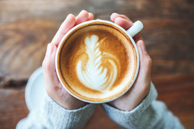 Cropped hand of woman holding coffee cup on table