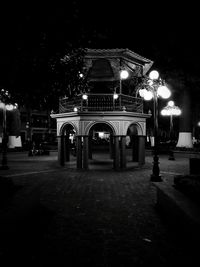 Illuminated street lights on footpath by building at night