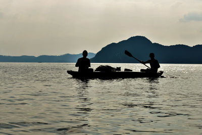 Silhouette men on boat fishing in lake against sky