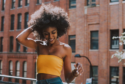 Happy young woman with afro hairstyle standing on bridge against building