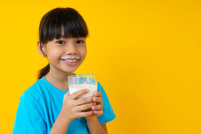 Portrait of smiling boy holding drink against yellow background