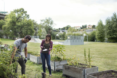 Mid adult man and woman examining plants in urban garden