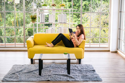 Asian girl making online payment using digital tablet at living room sofa at home