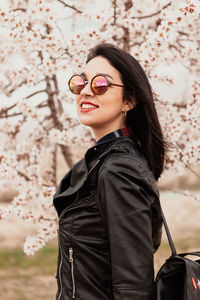 Smiling young woman looking away while standing against tree