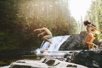 Cheerful friends jumping into river in forest