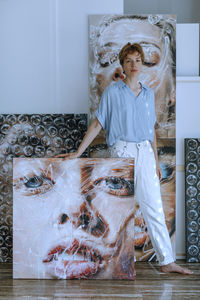 Confident mid adult female artist standing with various paintings in art studio