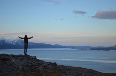 Rear view of man standing on rock against sky during sunset