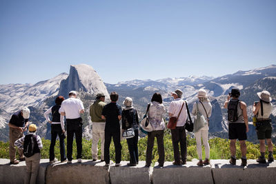 Rear view of people looking at mountains against clear blue sky