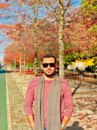 Portrait of young man wearing sunglasses standing by tree