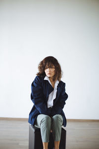 Portrait of young woman sitting against wall