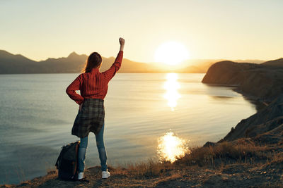 Rear view of person standing at beach during sunset