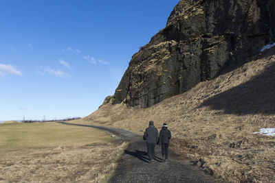 Rear view of friends walking on footpath against mountain