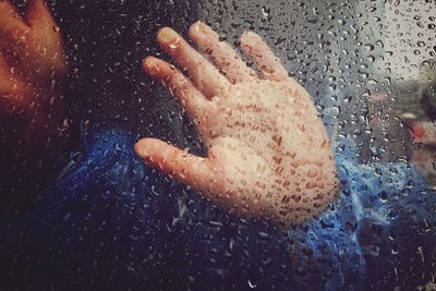 Cropped hand on wet glass during rainy season