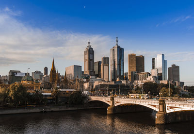 Bridge over river by buildings against sky in city