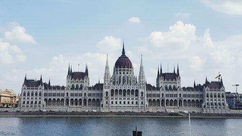 View of cathedral by river against cloudy sky