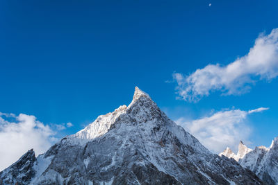 Low angle view of snowcapped mountains against blue sky