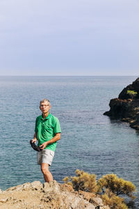 Portrait of man standing on rock by sea against sky