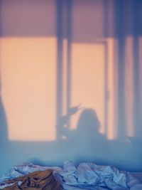 Rear view of woman sitting on bed against wall