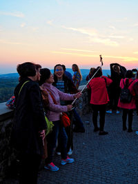 Group of people standing on land against sky during sunset