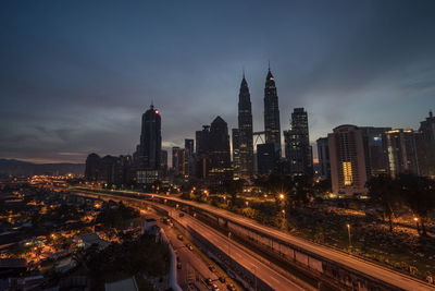 High angle view of bridge by petronas towers against cloudy sky at night