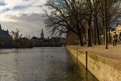 View of buildings by river against cloudy sky