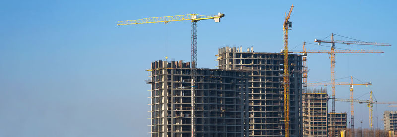 Low angle view of crane by building against clear blue sky