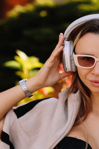 Portrait of a woman's face in sunglasses and wireless headphones walking in the city in autumn