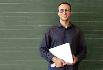 Portrait of man using digital tablet while standing against wall